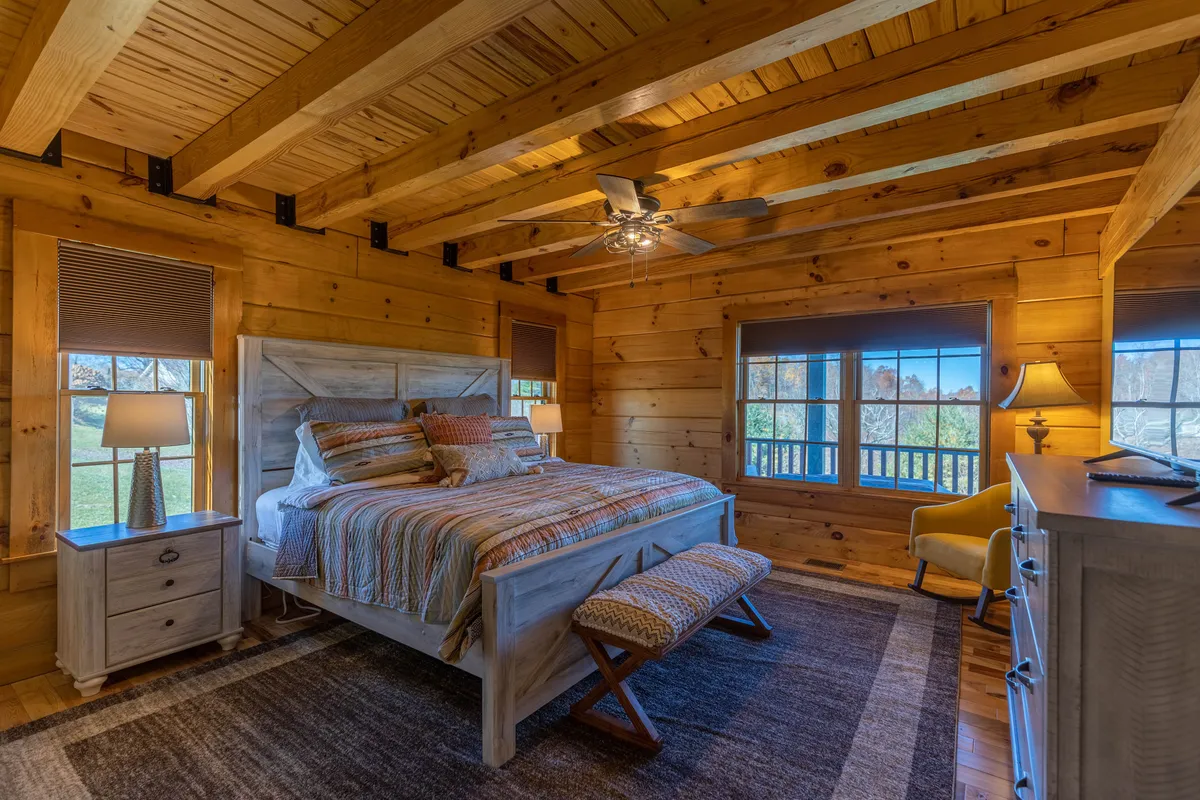 A tranquil bedroom with a cozy bed, large windows allowing in natural light, nightstands with lamps, and a ceiling fan overhead. The atmosphere is serene, ideal for restful sleep or quiet reading.