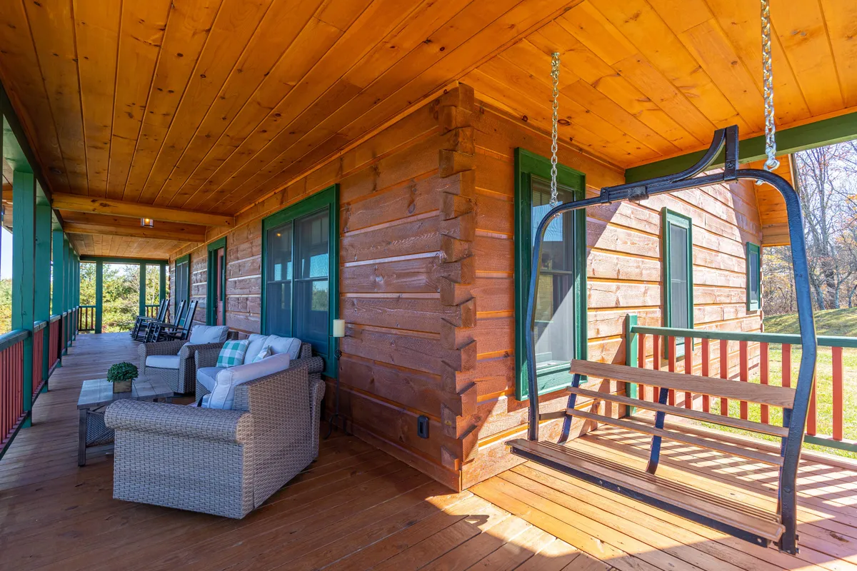 A spacious wooden porch with a swinging bench and ample outdoor seating, surrounded by lush greenery. The comfortable arrangement and open-air design make it a perfect spot for enjoying nature, socializing, or celebrating special moments under the stars.