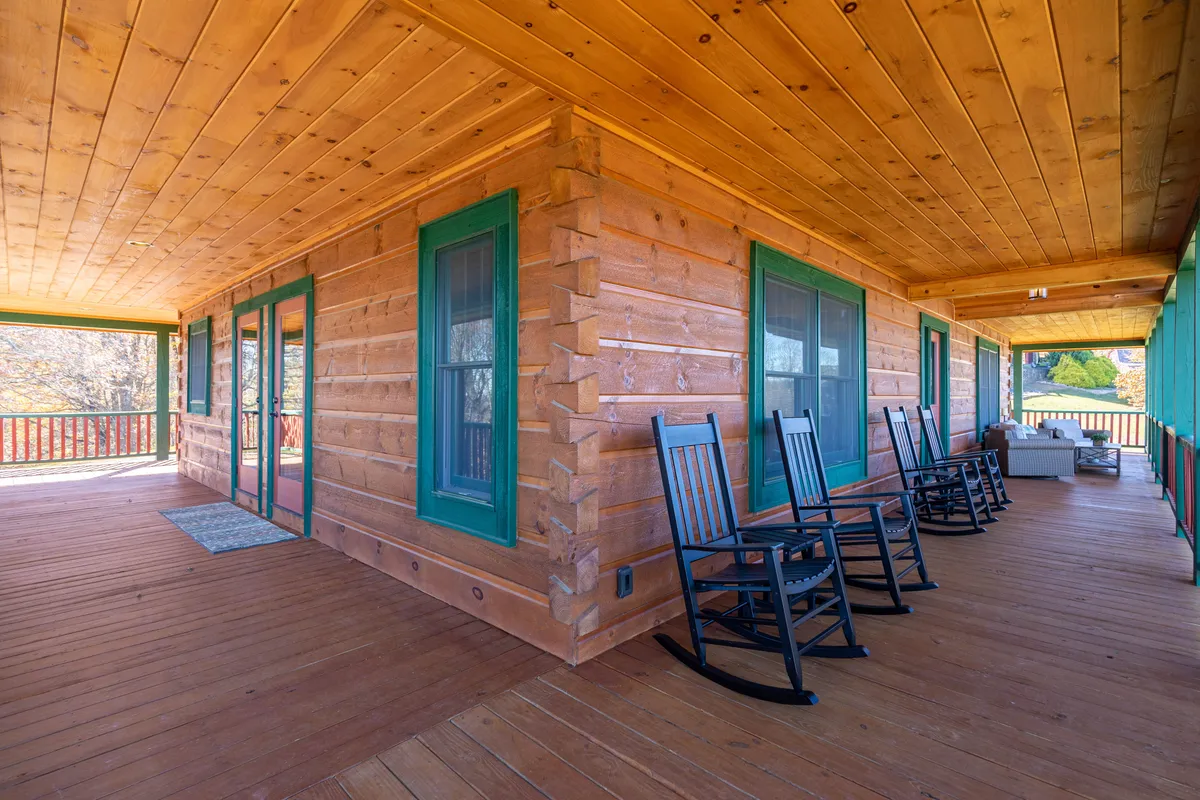 A cozy set-up on the porch featuring rocking chairs against log walls with green window frames, surrounded by the sights and sounds of nature. This area invites shared moments—be it sipping cocoa after a day out, relaxing with pets, or watching the sunset as a family.