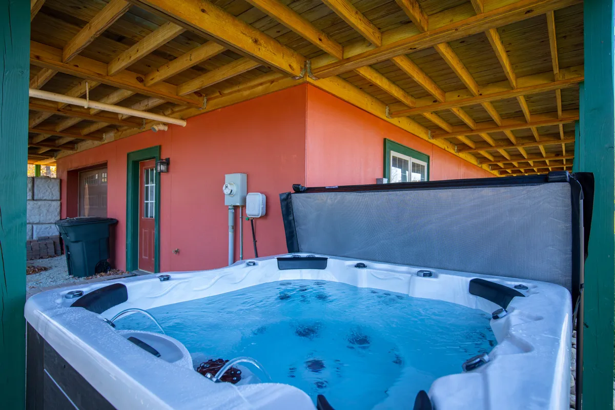 A cozy hot tub set beneath a wooden ceiling and next to a colorful wall, positioned outdoors for guests to relax while still connecting with the environment. The ambiance is inviting, ideal for soothing tired muscles after active days.