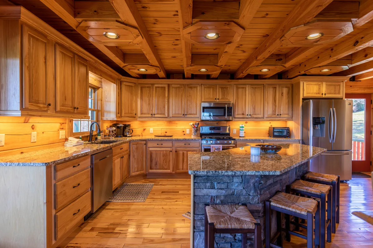 A bright kitchen scene showcasing sleek granite countertops, warm wooden cabinets, stainless steel appliances, and a stone bar area with comfortable seating. The open layout encourages group cooking, casual meals, and socializing.