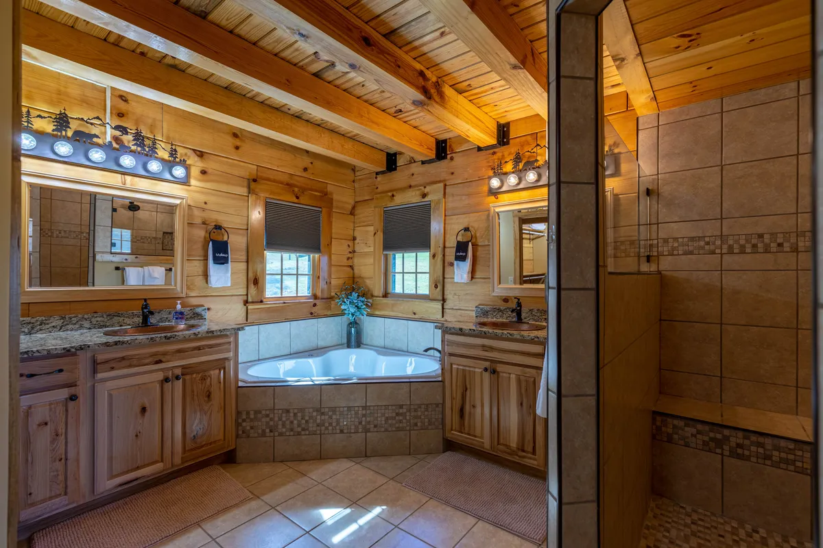 A spa-like bathroom featuring a jacuzzi tub, rustic wooden beams, mirrors, and a spacious sink area. The space feels luxurious and inviting, perfect for relaxation after a day outdoors.