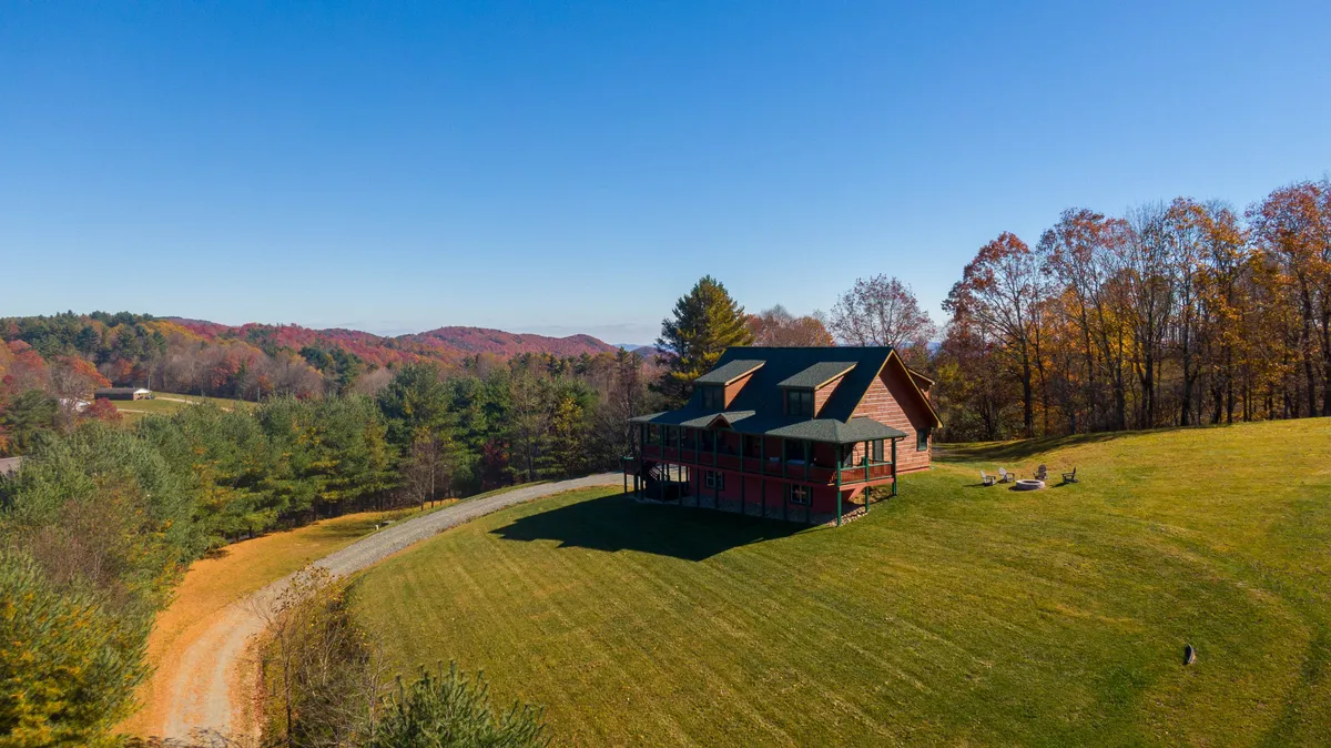 A wide exterior shot shows the house with its expansive deck, green lawn, and a stone fire pit in the foreground. Mountains stretch in the distance, and the yard provides ample space for pets or kids to play.