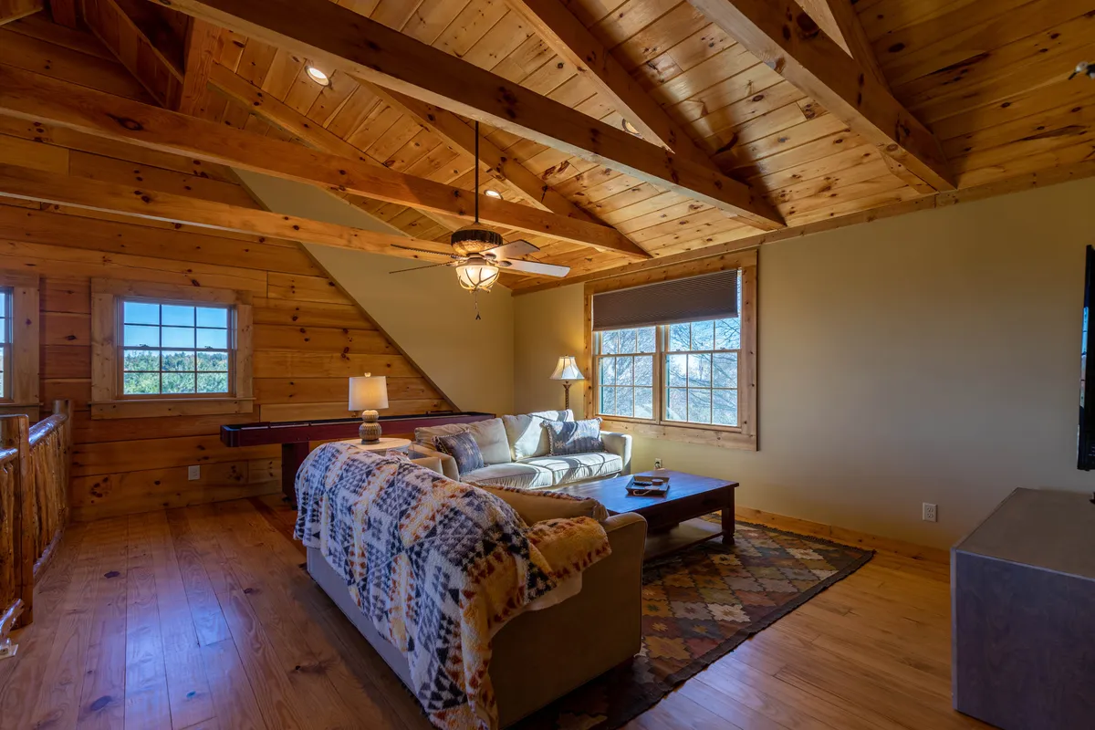 A bright, inviting sitting area with a cozy sofa, a central coffee table for games or snacks, large windows flooding the space with light, and a ceiling fan overhead. The setting is casual and friendly, ideal for games, reading, and social gatherings.