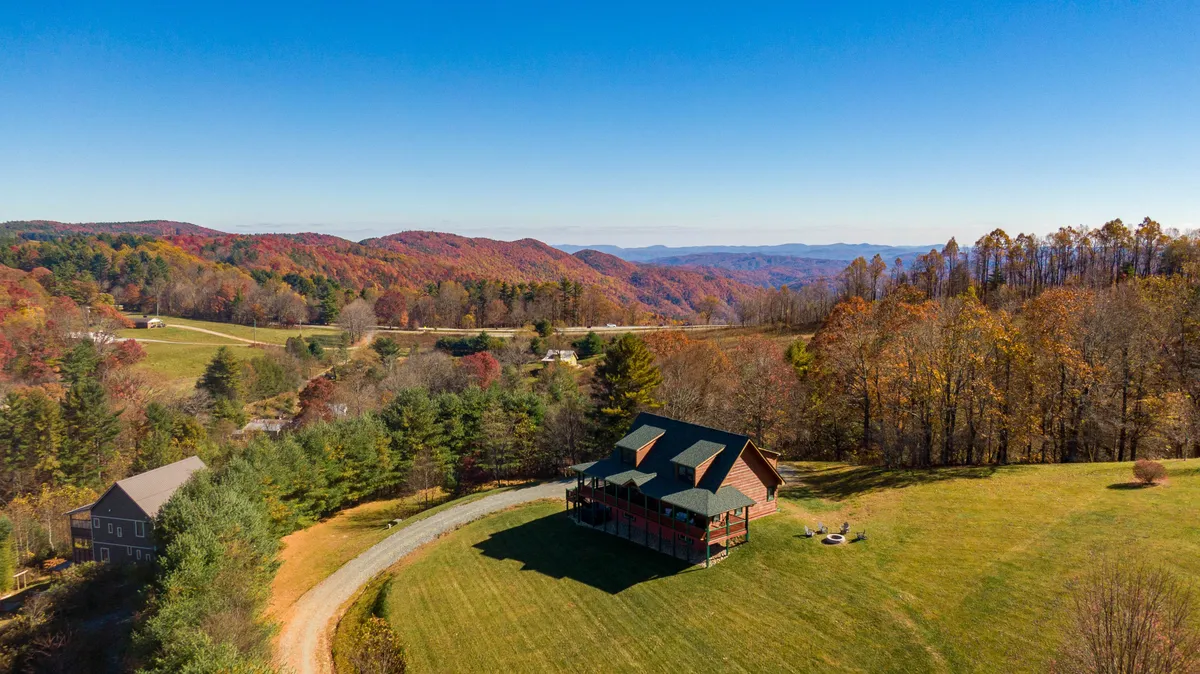 This image features the house set against the backdrop of rolling mountains and a spacious driveway. The natural landscape surrounding the property is visible, evoking a sense of peace and adventure. The view highlights both the accessibility of the home and its proximity to spectacular mountain scenery.