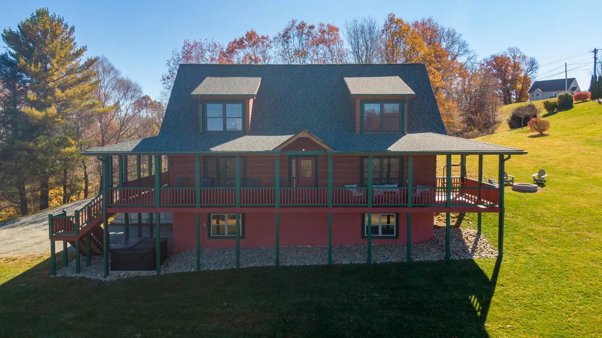 This exterior shot shows the large front porch with green railing, surrounded by a landscaped yard and mature trees. The generous outdoor space is inviting and spacious, ideal for families and pets to play safely. The fenced deck and the view of the open yard reinforce the pet-friendly, family-focused atmosphere.