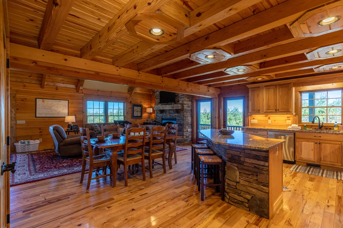 A dining area with a spacious table, breakfast bar, and a fireplace, all framed by large windows that offer glimpses of the outdoors. The layout encourages family meals and socializing, with a sense of connection to the exterior landscape.