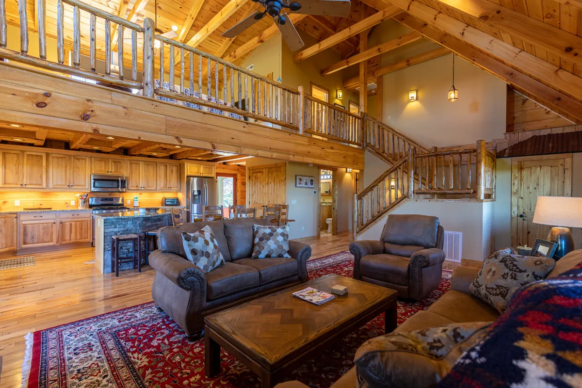 A welcoming open-concept living area featuring exposed wooden beams, a large kitchen counter, and a cozy seating arrangement centered around a fireplace. The space evokes warmth and togetherness, perfect for gathering after a day of mountain exploration.